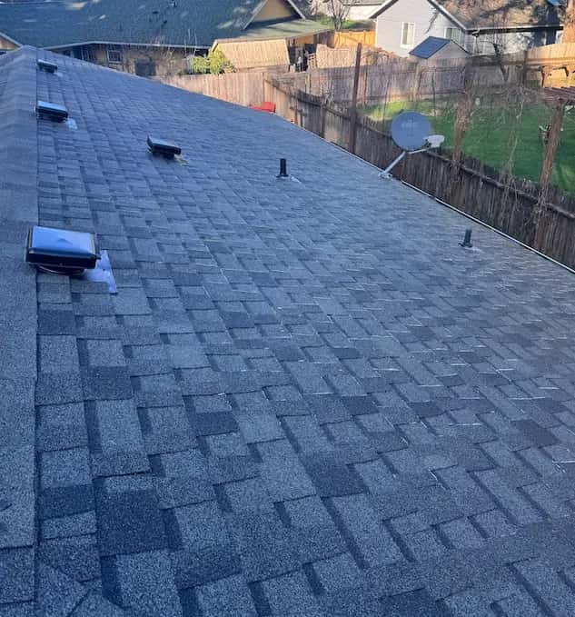 Clean gray composition shingle roof with box vents and a satellite dish, overlooking a fenced backyard.