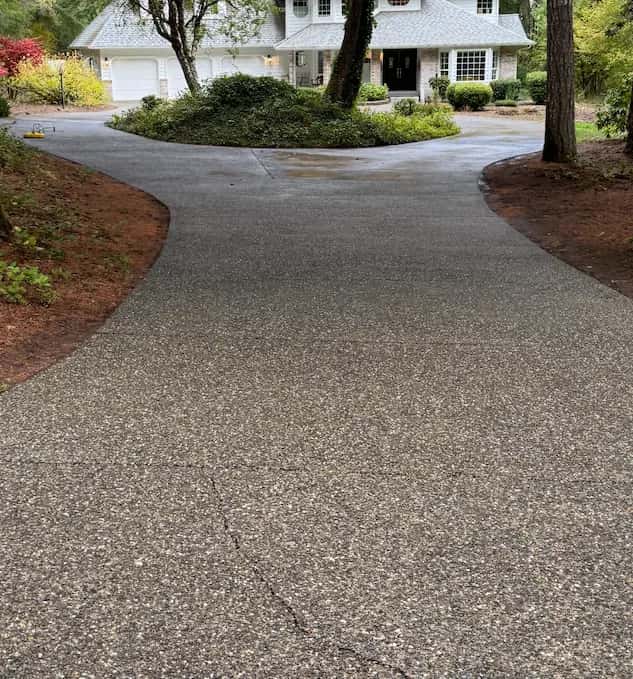 Freshly cleaned exposed-aggregate driveway curving around a landscaped island to a large two-story home.